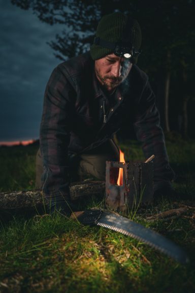 Mann mit Stirnlampe, der am Boden arbeitet, während ein Feuer brennt.